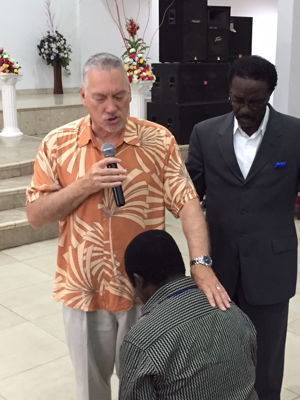 Man praying, another man standing over him with hand on shoulder 
